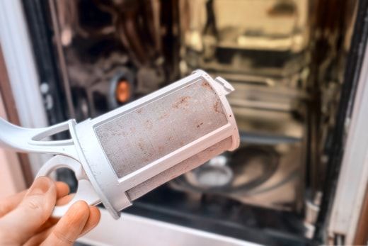 Removable dishwasher filter showing trapped food debris before cleaning.